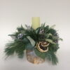 A round candle arrangement with seasonal foliage, cone, dried fruit ad a matching candle.
